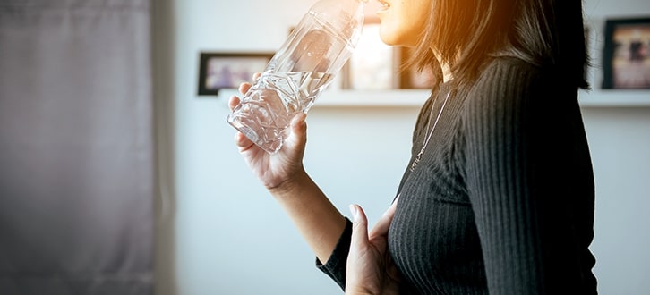 mujer en casa bebiendo agua para ayudar con la acidez estomacal