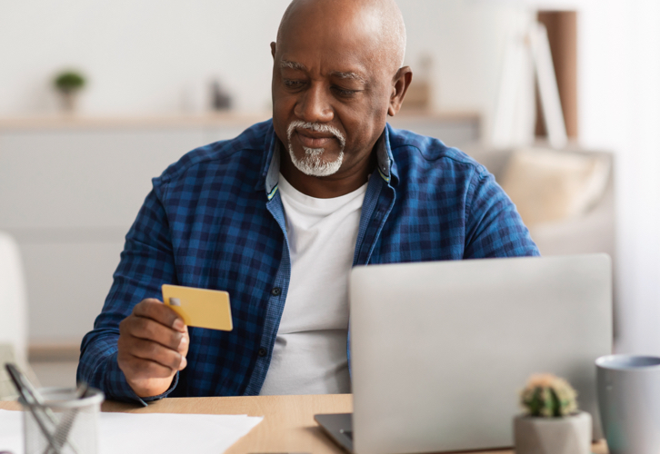 Un hombre mayor con su computador portátil sosteniendo su tarjeta de crédito